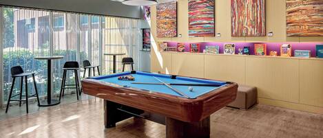 A pool table in a room with large windows, bar stools, and colorful artwork on the walls.