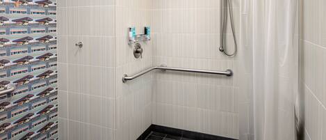 A shower area with a handrail, a showerhead, and a tiled floor.