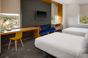 Habitación de hotel con escritorio, dos camas, televisión y vistas al exterior.