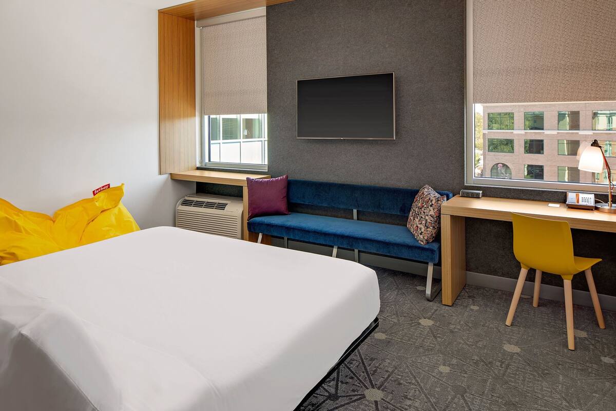 A hotel room with a bed, a desk, a chair, a sofa, and a TV.