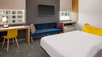 Une chambre d’hôtel moderne équipée d’un lit, d’un bureau, d’une chaise, d’un canapé et d’une grande fenêtre.