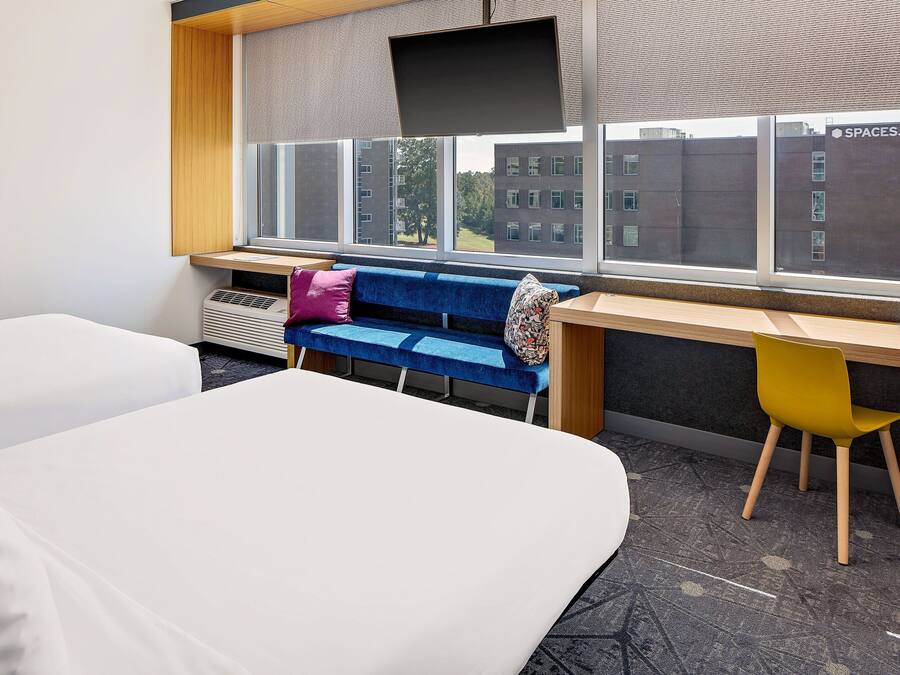 Quarto de hotel com cama, sofá azul, cadeira amarela e escrivaninha.