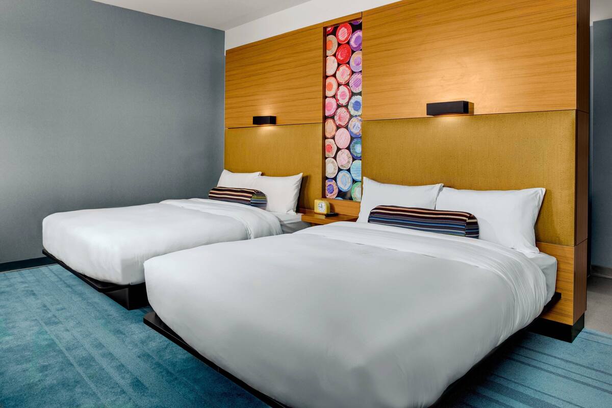 A hotel room with two beds, a wooden headboard, a blue carpet, and a wall with a colorful circular design.