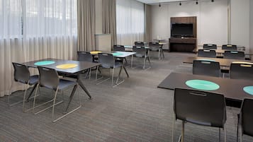 Uma sala de conferência com mesas, cadeiras, uma televisão e uma lareira.