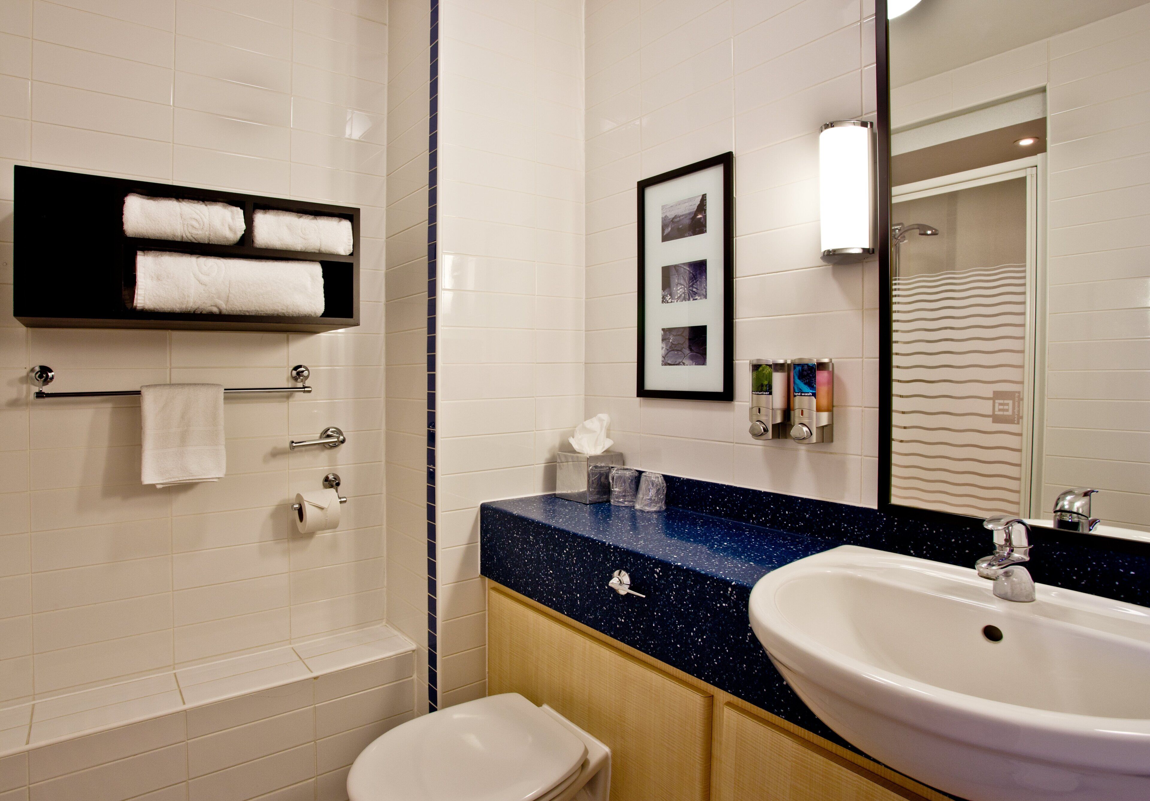 A bathroom with a white sink, a mirror, a framed picture, and a towel rack with towels.