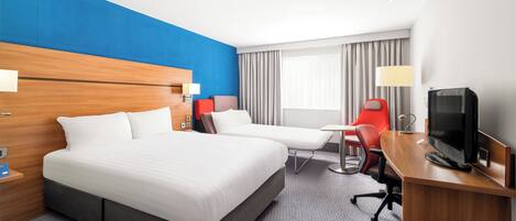 A hotel room with a large bed, a desk with a TV, a red chair, and a window with curtains.