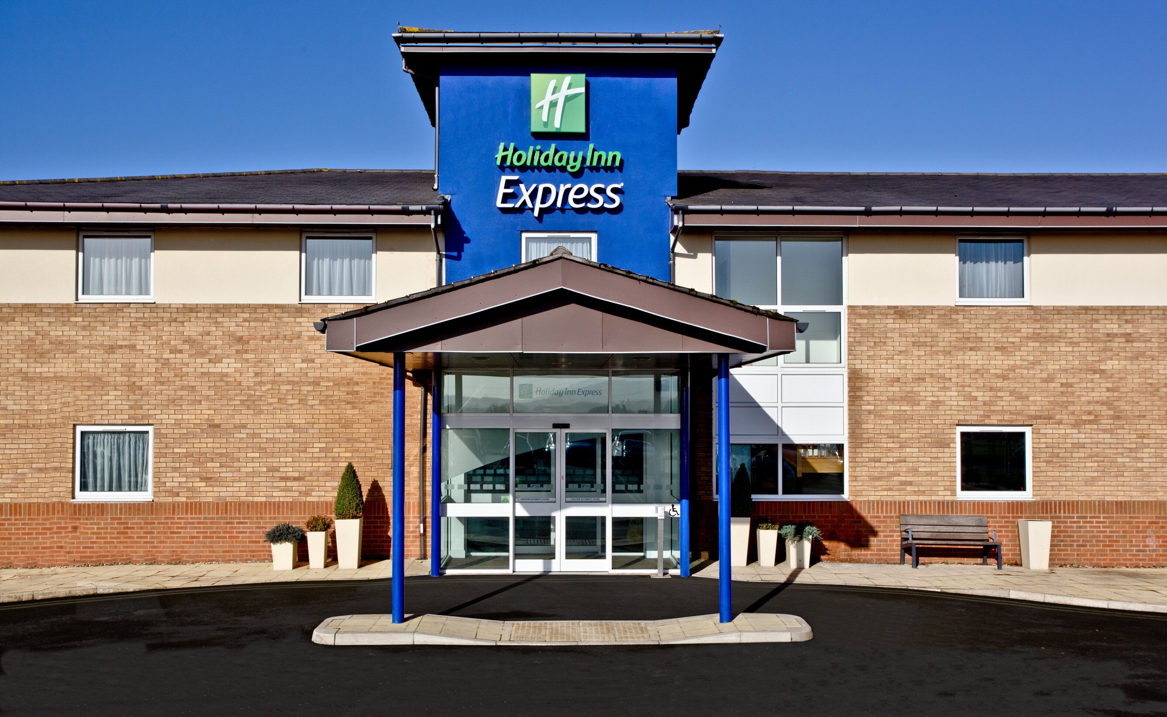 A Holiday Inn Express building with a clear entrance, a covered waiting area, and a brick facade.