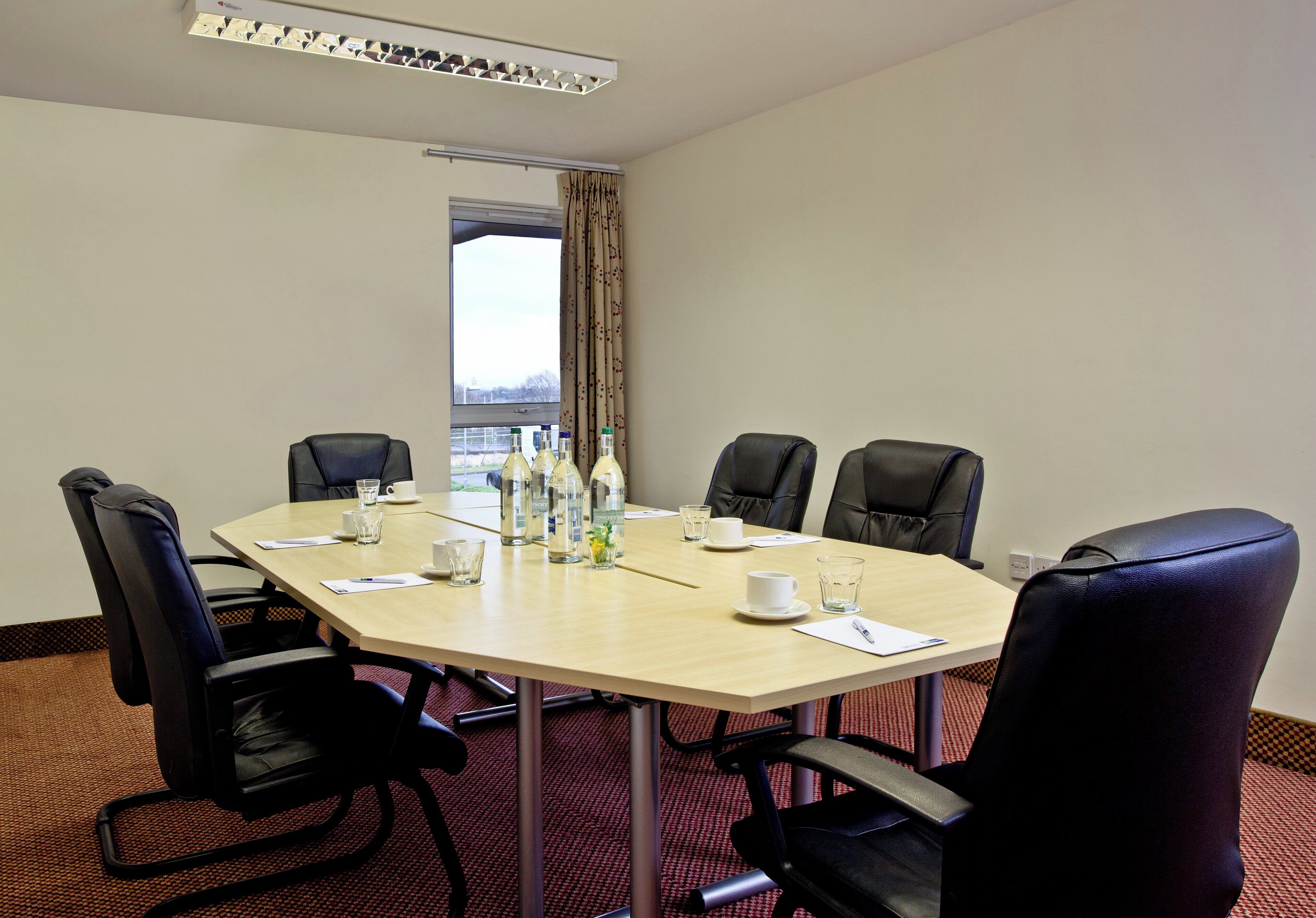A conference room with a round table, six black chairs, and various items like water bottles, cups, and papers.