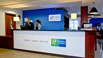 En receptionsdisk på ett Holiday Inn Express-hotell, med en blå vägg, en digital skärm och en skylt som visar hotellets namn.