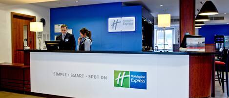 A Holiday Inn Express reception desk with a blue wall, a digital screen, and a sign indicating the hotel's name.