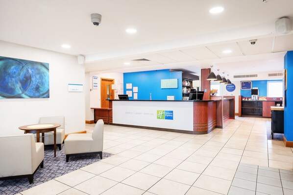 A hotel reception area with a blue wall, a reception desk, and seating arrangements.