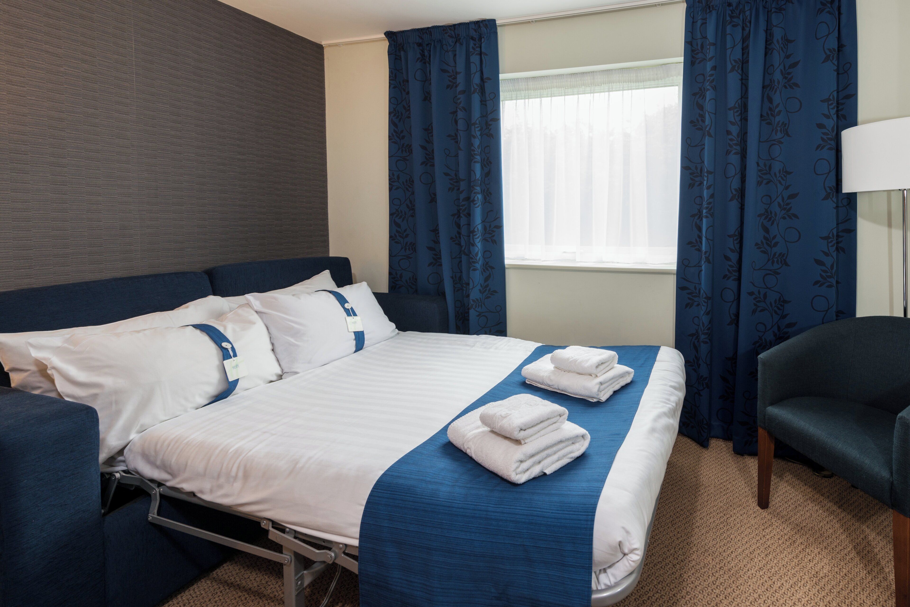 A hotel room with a bed, a chair, and a window with curtains.