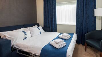 A hotel room with a bed, a chair, and a window with curtains.
