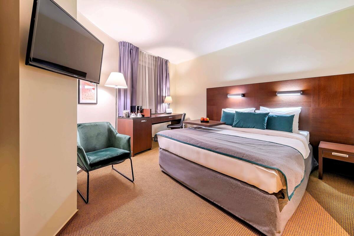 A hotel room with a bed, a desk, a chair, a TV, and a window with curtains.