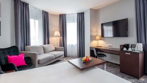Habitación de hotel con cama, sofá, escritorio, televisor y cafetera.
