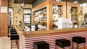 Zona de bar con mostrador, taburetes y estantes llenos de botellas.