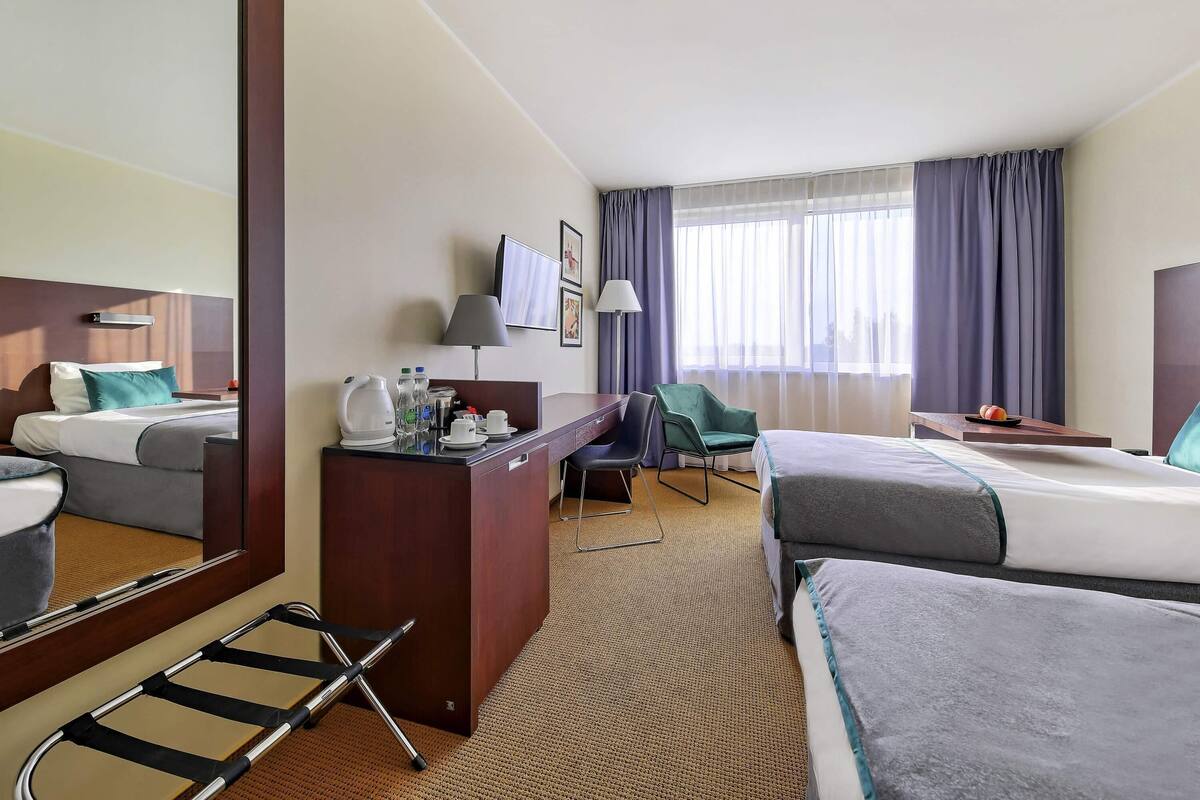 A hotel room with a bed, desk, chair, and a large mirror.