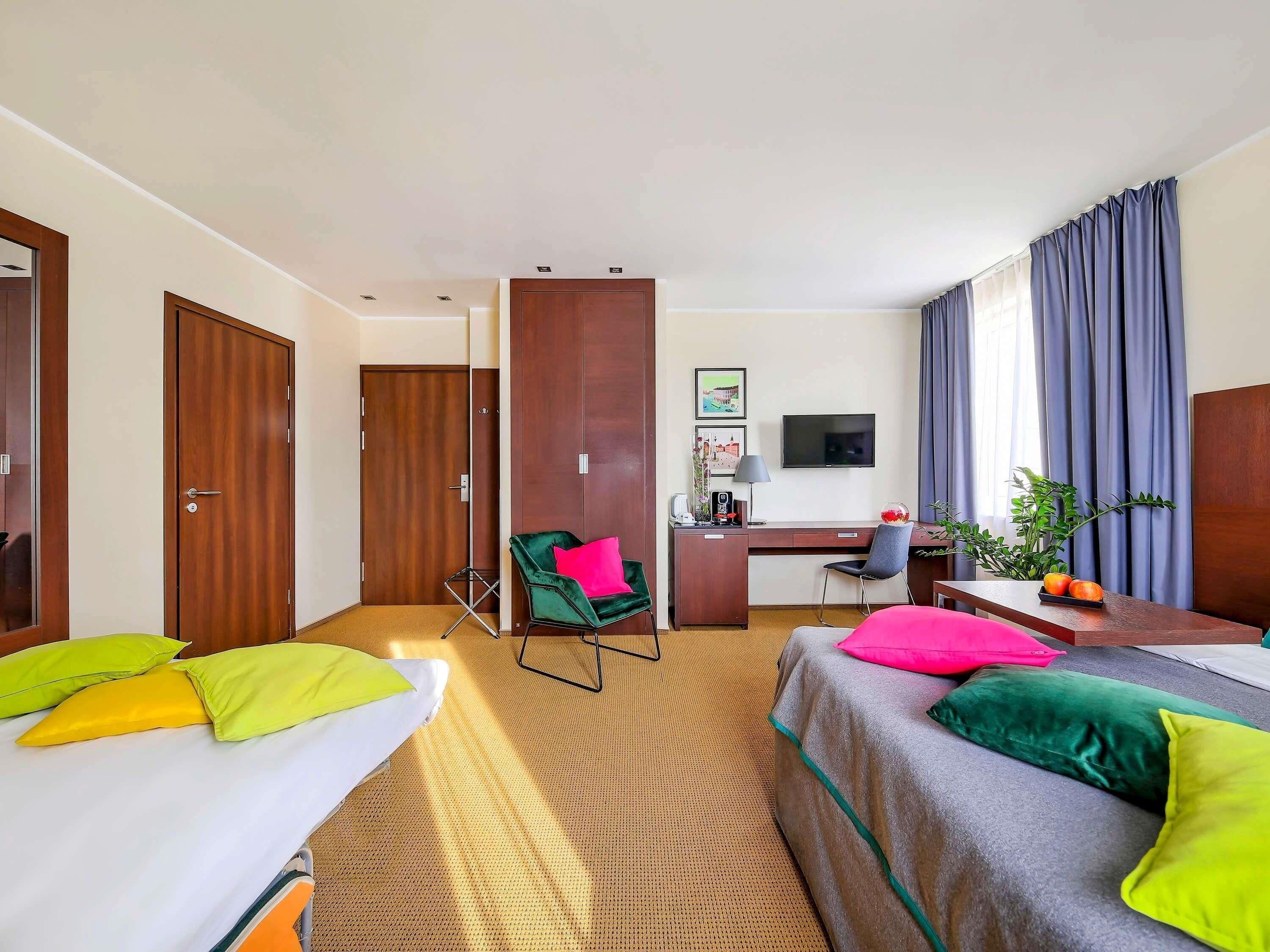 Habitación de hotel con dos camas, un escritorio, una silla, un televisor y una ventana con cortinas.