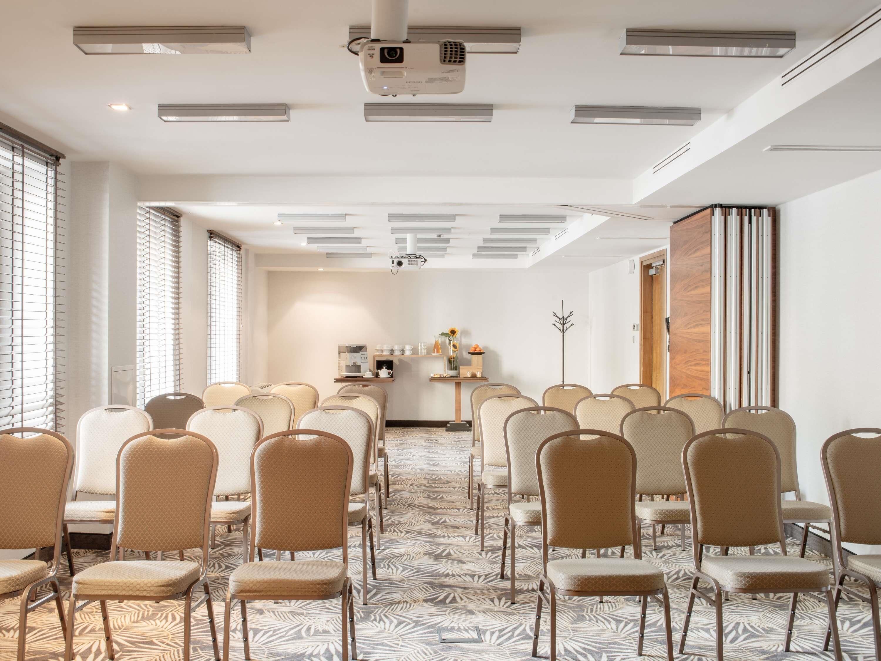 Un salón de conferencias con filas de sillas, un proyector y una estación de café.