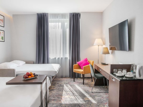 Ein Hotelzimmer mit zwei Betten, einem Schreibtisch mit Stuhl, einem Fernseher und einer Kaffeemaschine.