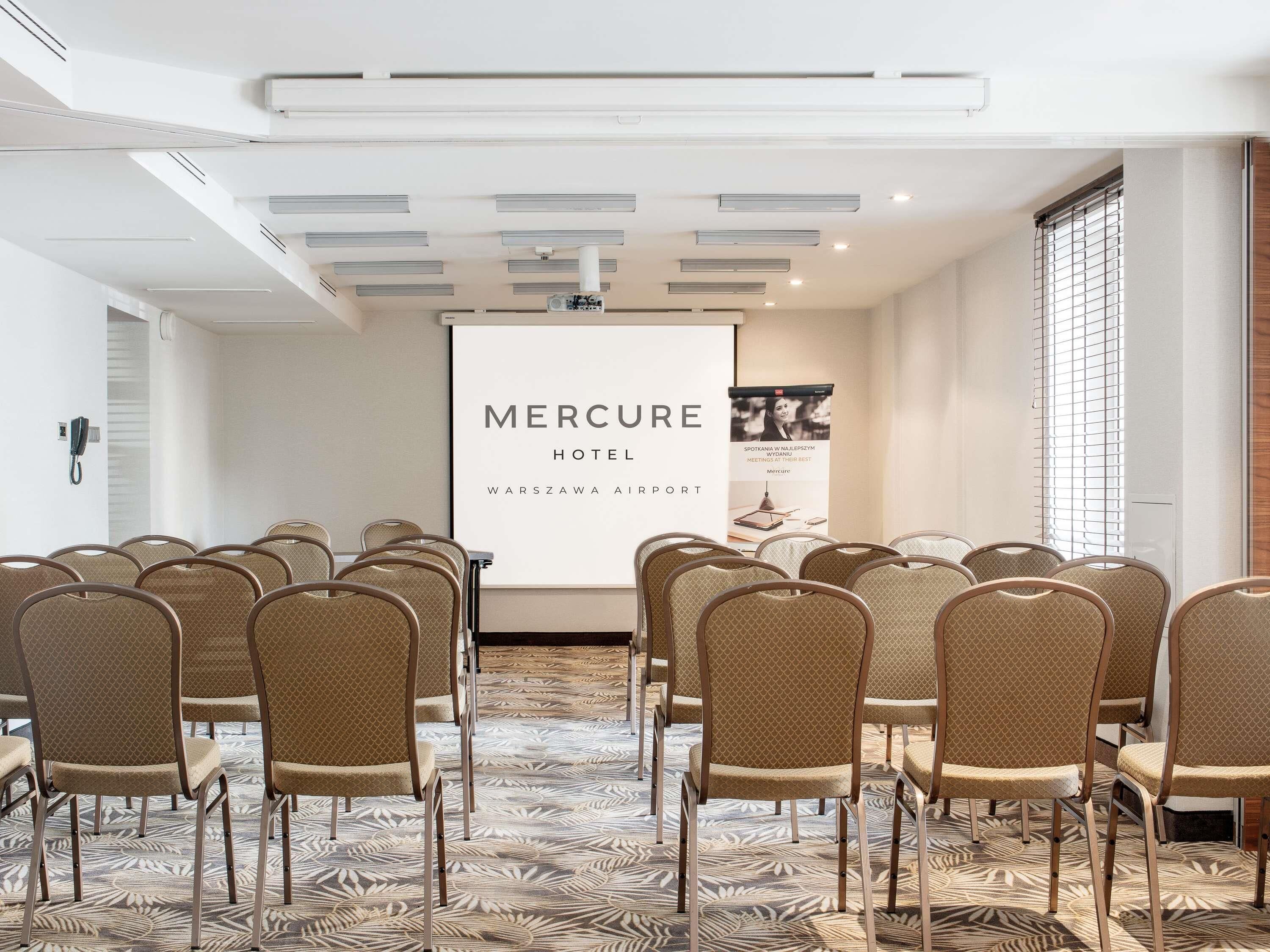 A conference room at Mercure Hotel with rows of chairs facing a presentation screen.