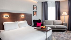 Una habitación de hotel con cama, escritorio con fruta, sofá y lámpara.