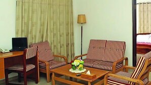 Habitación de hotel con un escritorio, dos sillones a rayas, un sofá, una mesa de centro con un arreglo floral y una lámpara.
