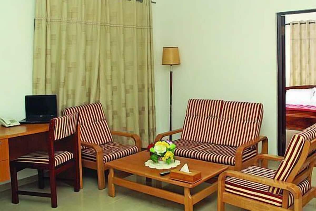 A hotel room with a desk, two striped armchairs, a sofa, a coffee table with a flower arrangement, and a lamp.