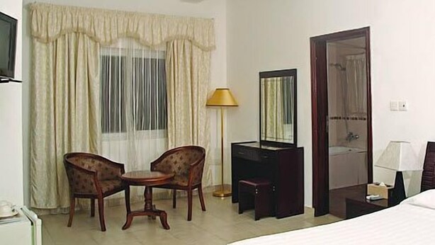 Habitación de hotel con cama, escritorio, dos sillas, espejo y ventana con cortinas.