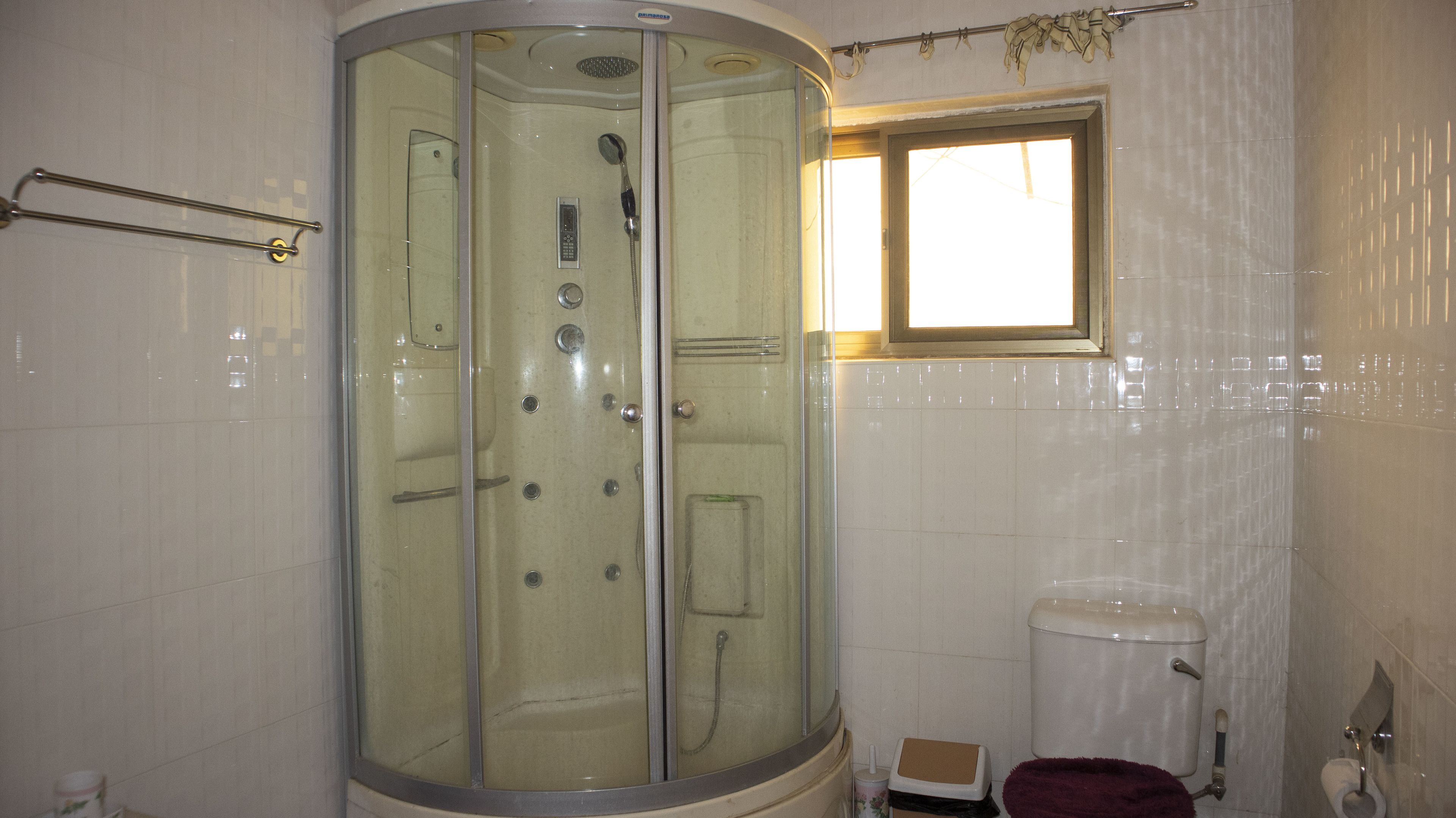 Un baño con ducha de vidrio, inodoro y ventana que deja entrar luz natural.