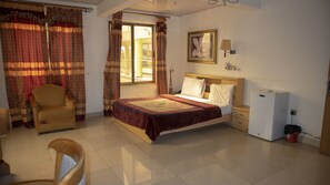 A bedroom with a bed, a chair, a nightstand, a lamp, a mirror, and a refrigerator. - Crown Liberty Hotel (Accra)