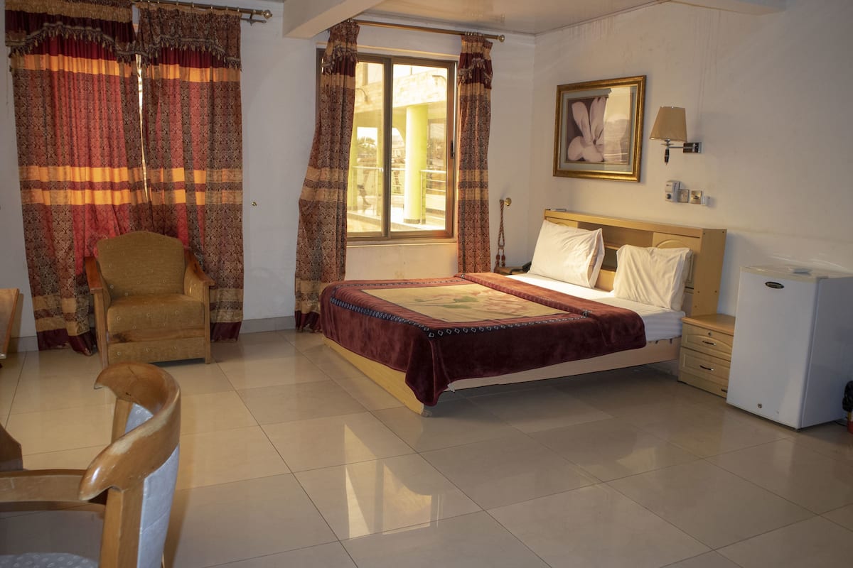 Une chambre à coucher avec un lit, une chaise, un bureau et une fenêtre avec des rideaux.