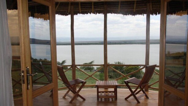 A wooden deck with two wooden chairs and a small table, overlooking a calm lake with a distant shoreline. - Elementaita Country Lodge (Nakuru)