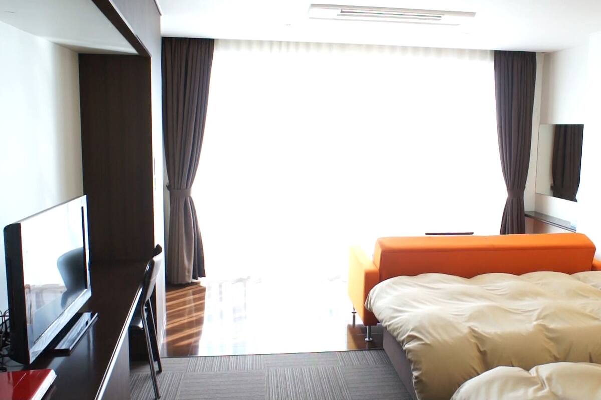 Una habitación de hotel con cama, televisión, escritorio y ventana con cortinas.