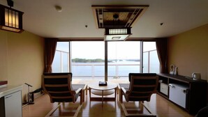 A room with a large window, a small round table, two striped chairs, a cabinet, and a ceiling light fixture. - Washuzan Shimoden Hotel (Kurashiki)