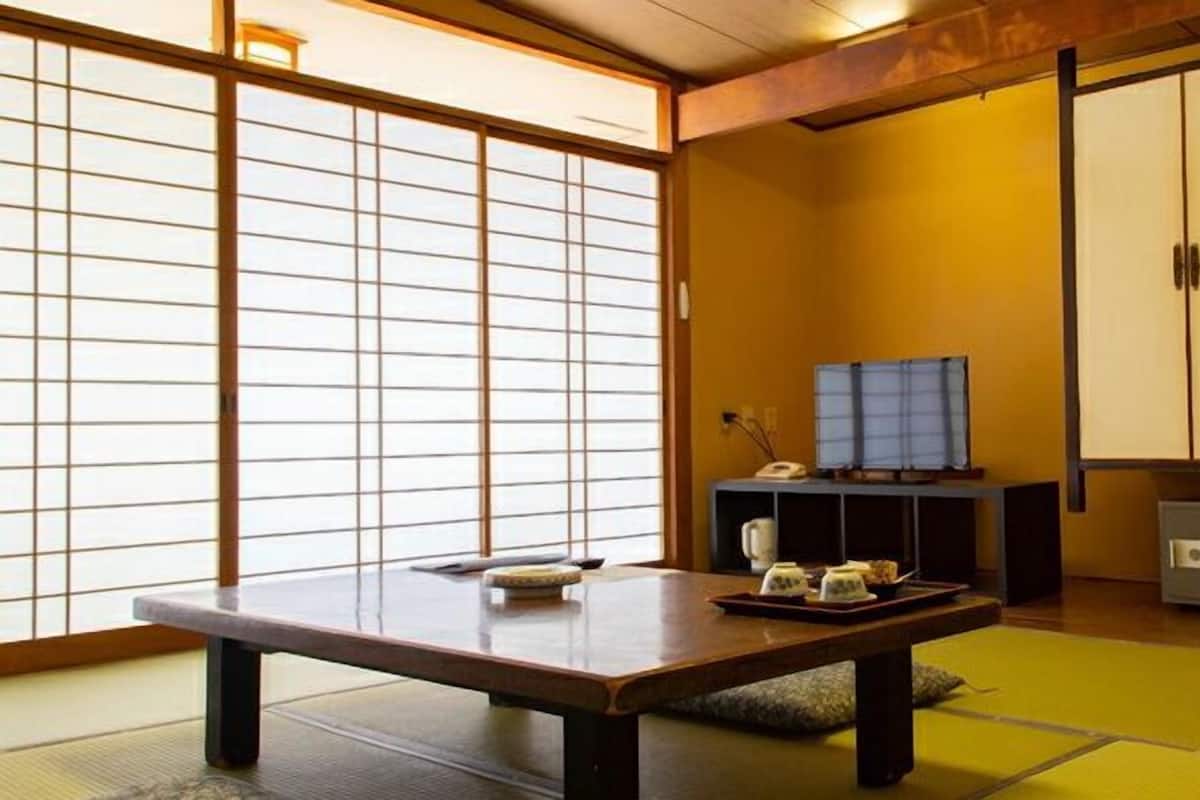 Una habitación japonesa tradicional con suelo de tatami, una mesa baja con juego de té, un televisor sobre un mueble y puertas correderas.