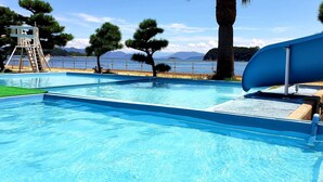 A swimming pool with a slide, surrounded by trees and a view of the sea. - Washuzan Shimoden Hotel (Kurashiki)