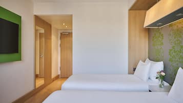 A hotel room with two beds, a flat-screen TV mounted on the wall, a wooden door, and a green patterned wall.