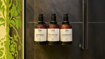 Tres botellas de artículos de baño de hotel: champú, gel de ducha y acondicionador, con la etiqueta 'nh hotels' y 'té verde'.