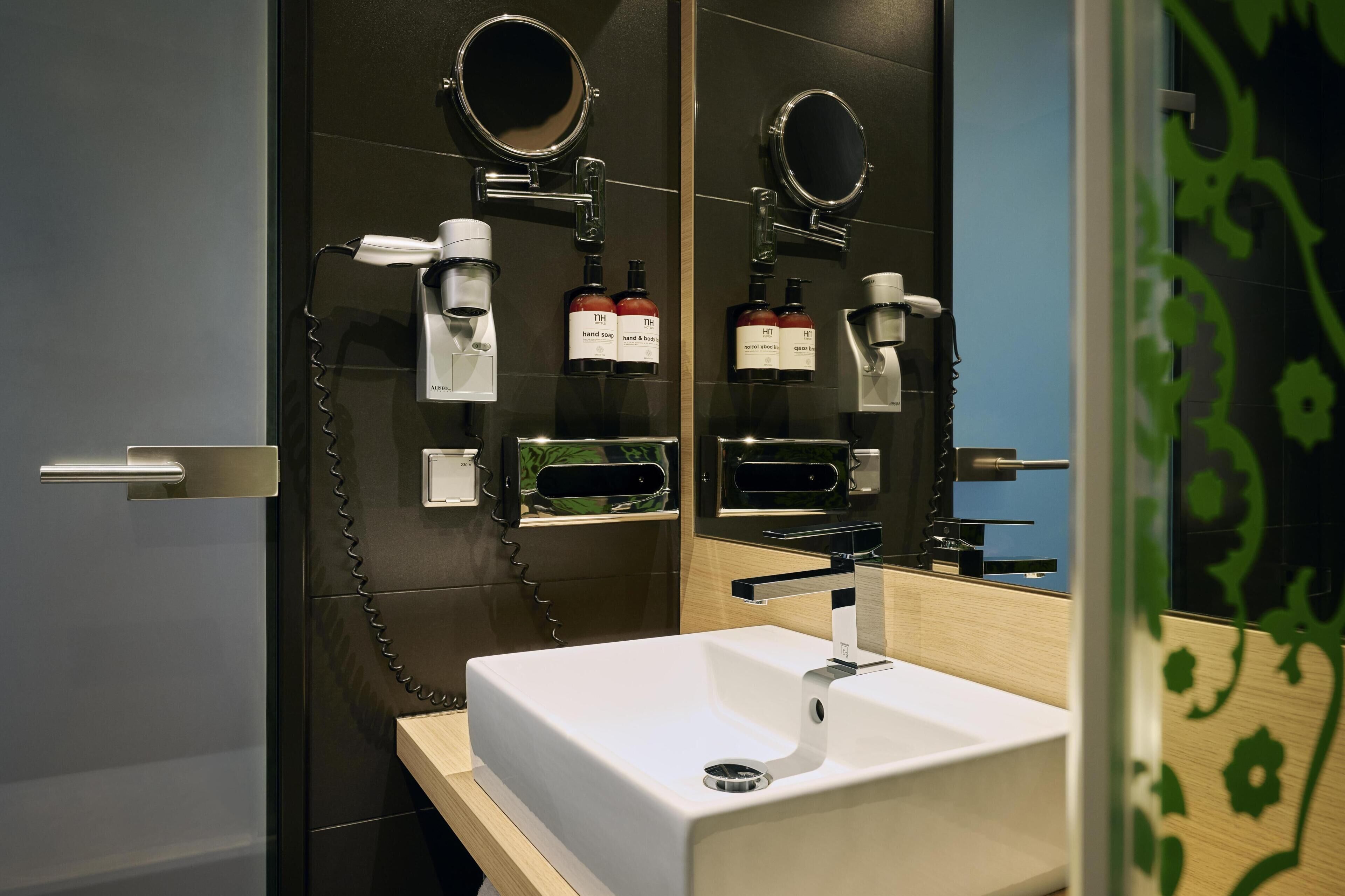 A modern bathroom with a white sink, a mirror, and a hairdryer mounted on the wall.