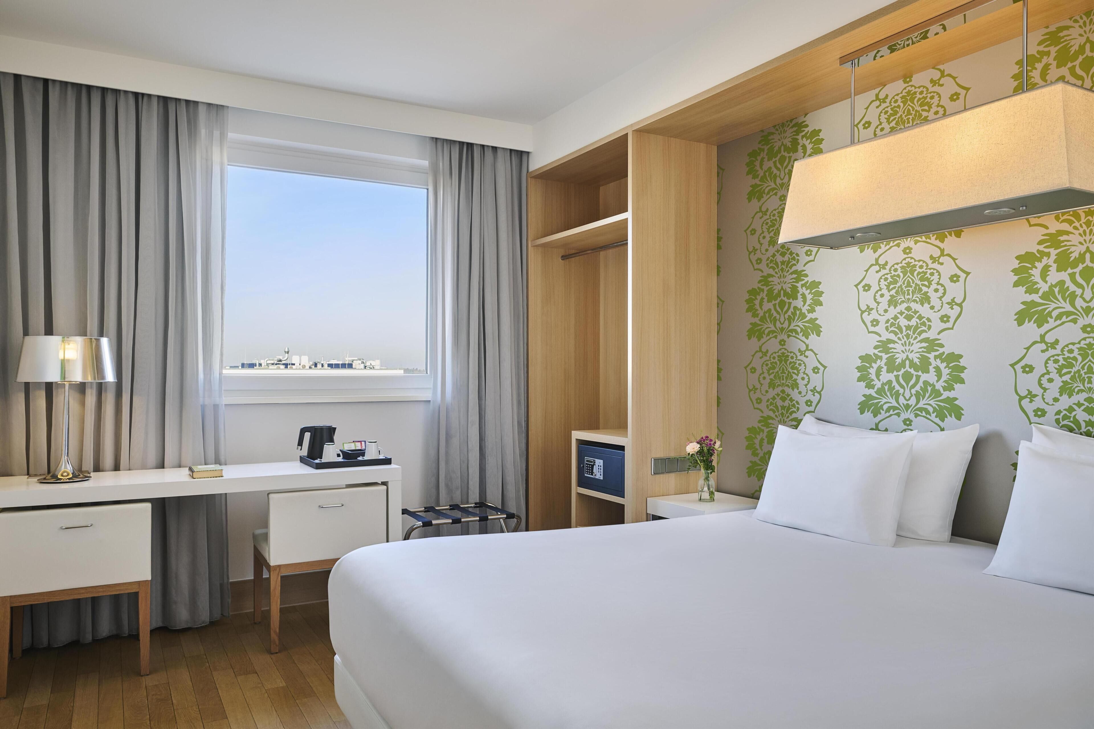 A hotel room with a bed, desk, chair, and a window with curtains.