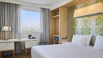 A hotel room with a bed, desk, chair, and a window with curtains.