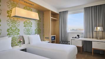 Una habitación de hotel con dos camas, un escritorio, una silla, una lámpara, una mesita de noche y una ventana con cortinas.