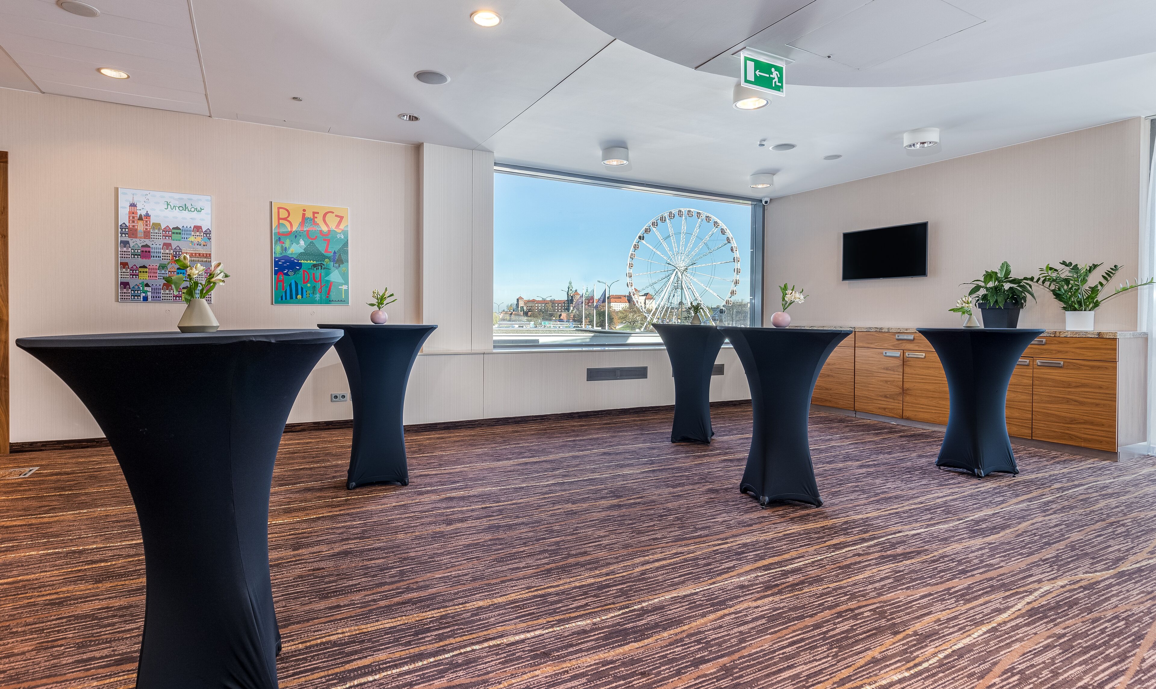 Une salle de conférence avec quatre tables noires, une grande fenêtre donnant sur une grande roue et un téléviseur fixé au mur.