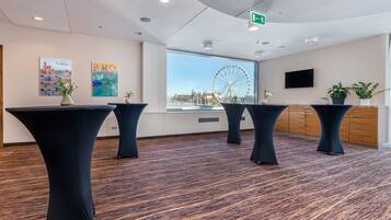 Une salle de conférence avec quatre tables noires, une grande fenêtre donnant sur une grande roue et un téléviseur fixé au mur.