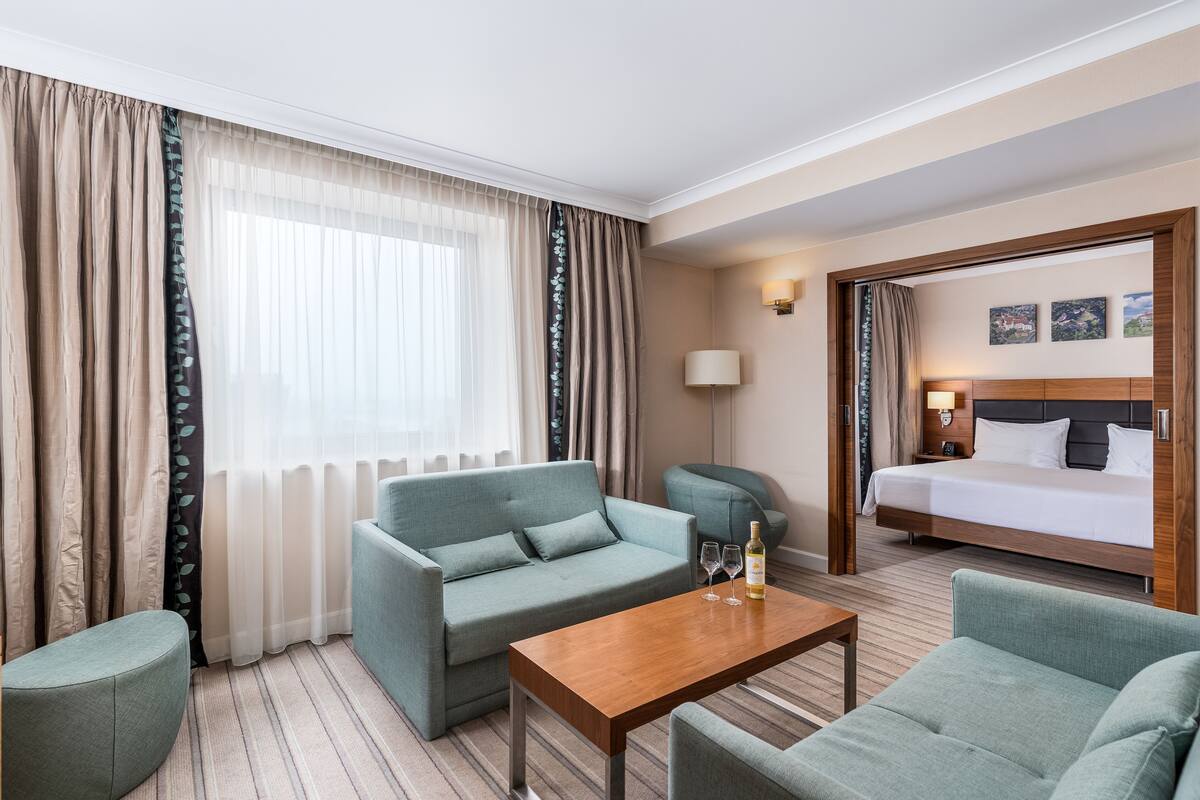 A hotel room with a bed, a sofa, a small table, and a lamp.