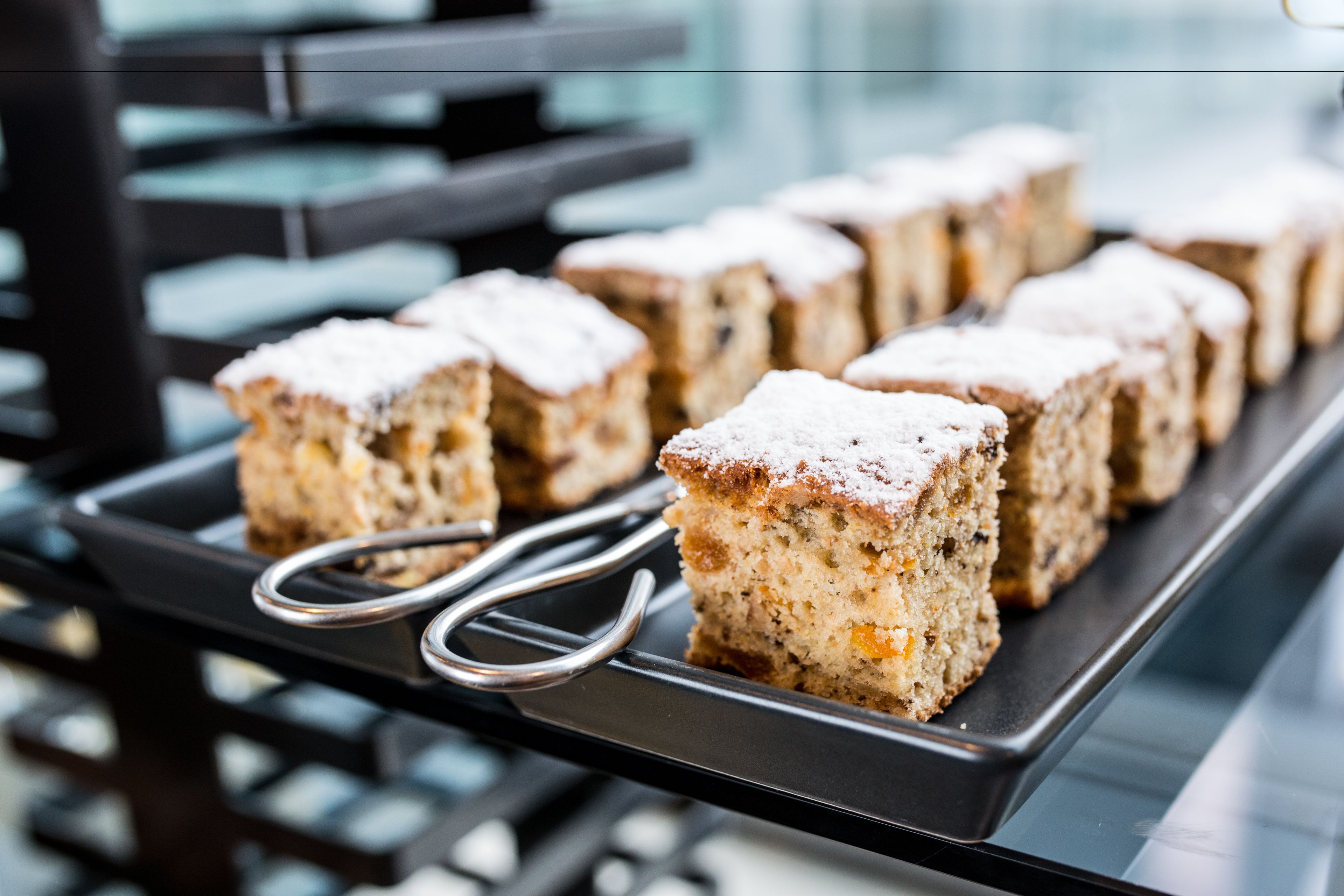 Un plat amb postres quadrades, decorades amb un pols de sucre, disposades sobre una estructura metàl·lica.