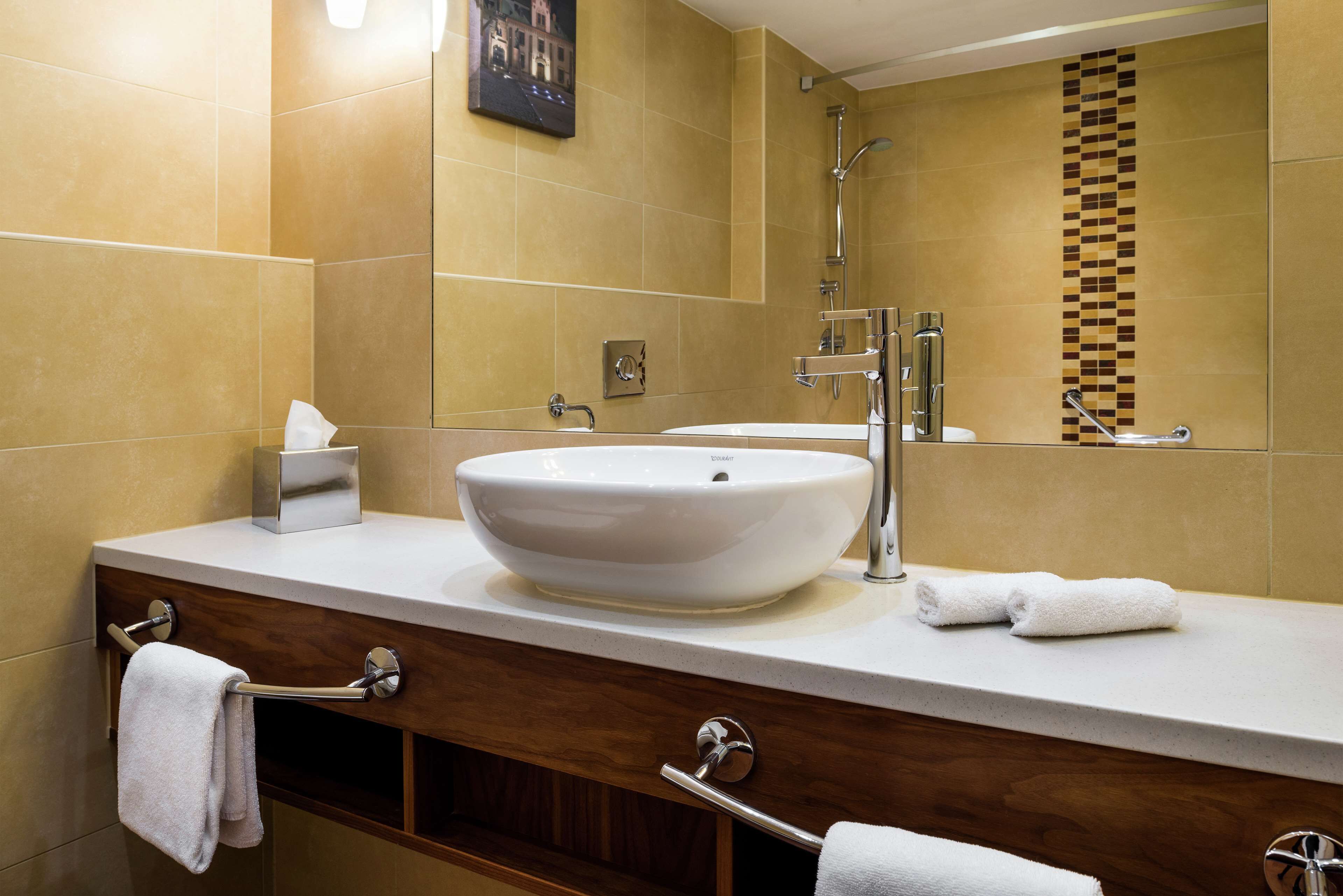 A modern bathroom with a large white sink, a mirror, and a shower.