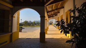 A covered outdoor area with arches, a tiled floor, and a view of a distant building. - Hospedium Hotel Cortijo Santa Cruz (Villanueva de la Serena)