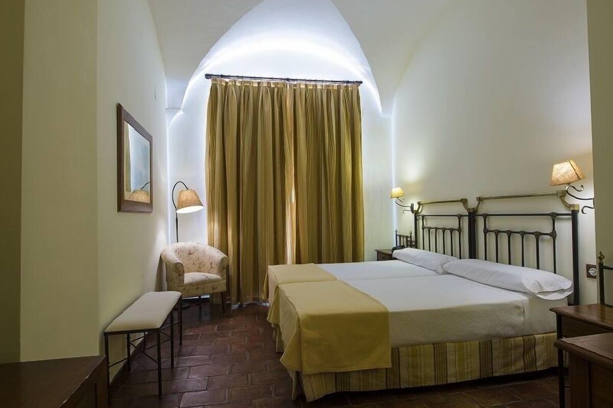 Ein Schlafzimmer mit Bett, Stuhl, Schreibtisch und einem Fenster mit Vorhängen.